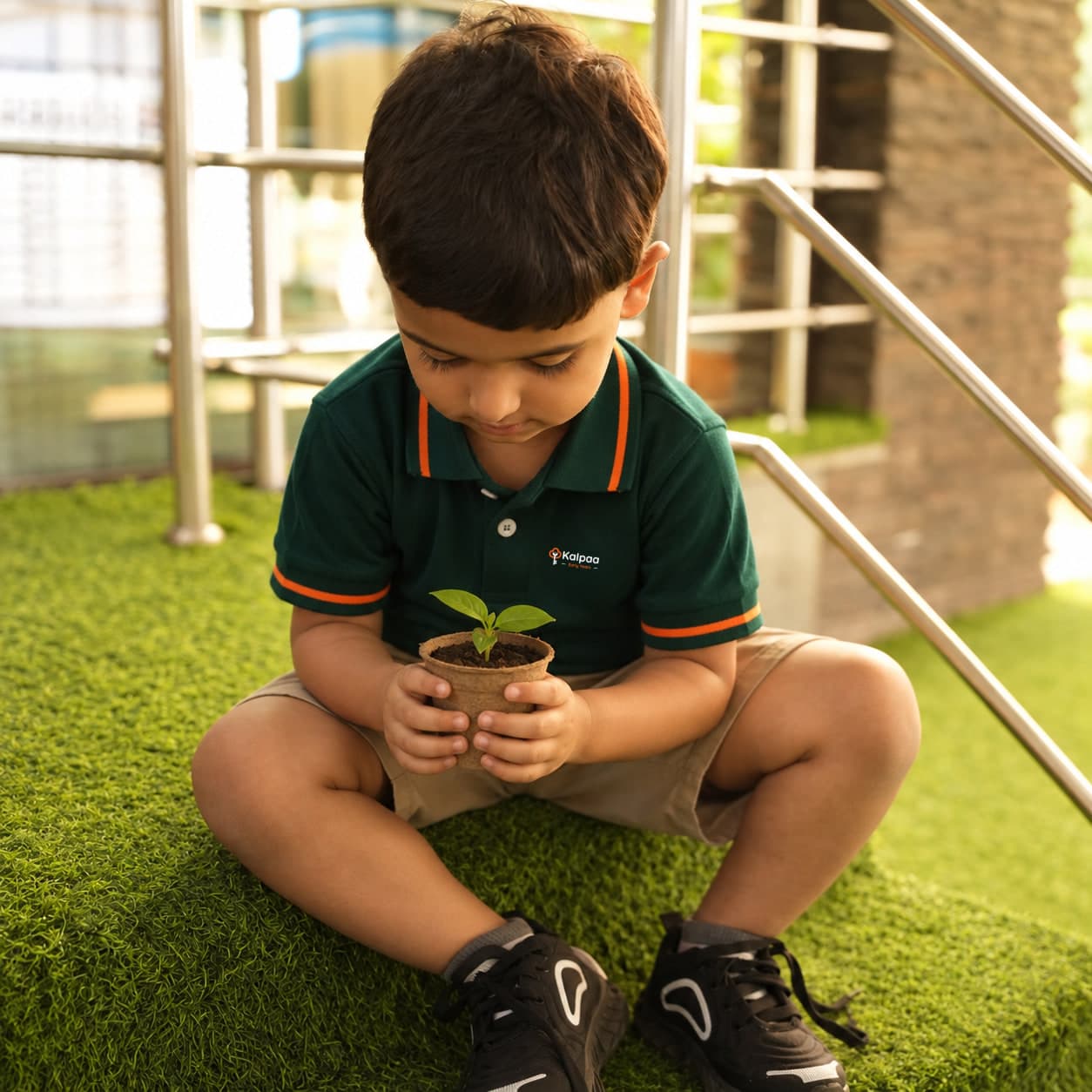 A child sitting on the grass, studying the seedling cupped in his hands