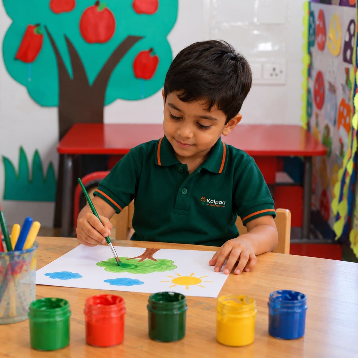 A child painting a tree, clouds and a sun with poster paints at the atelier table