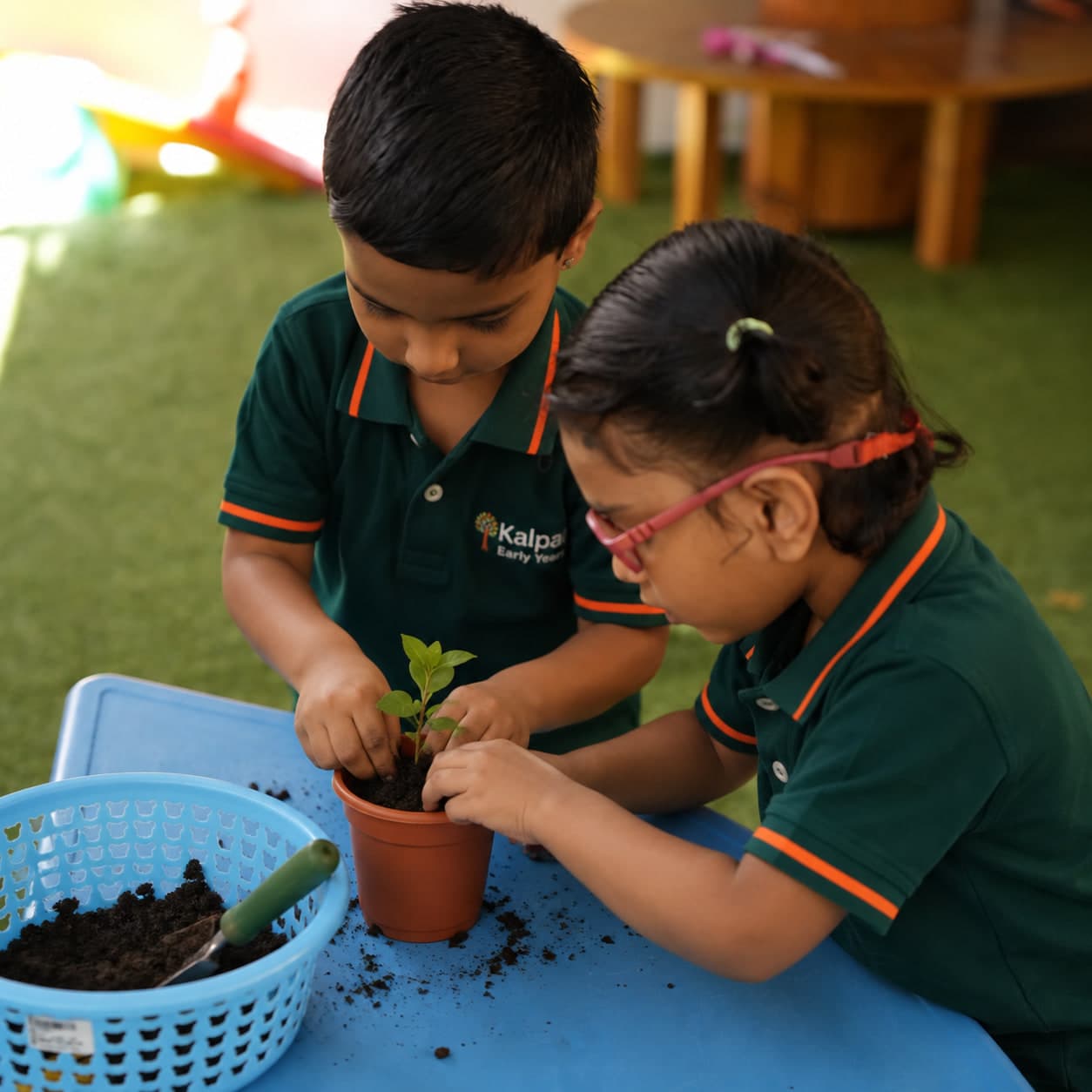Two children potting a seedling together at the garden table