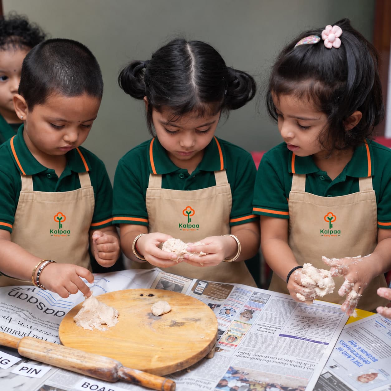 Three children in Kalpaa aprons working dough at the table