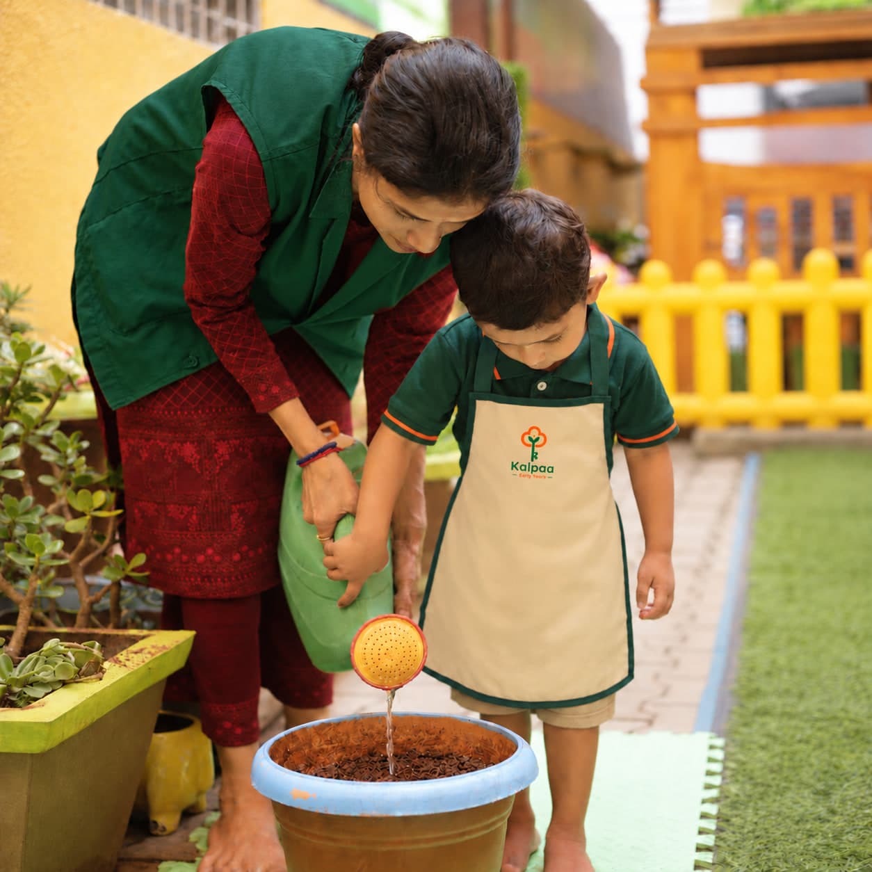A child watering the class pot with his teacher