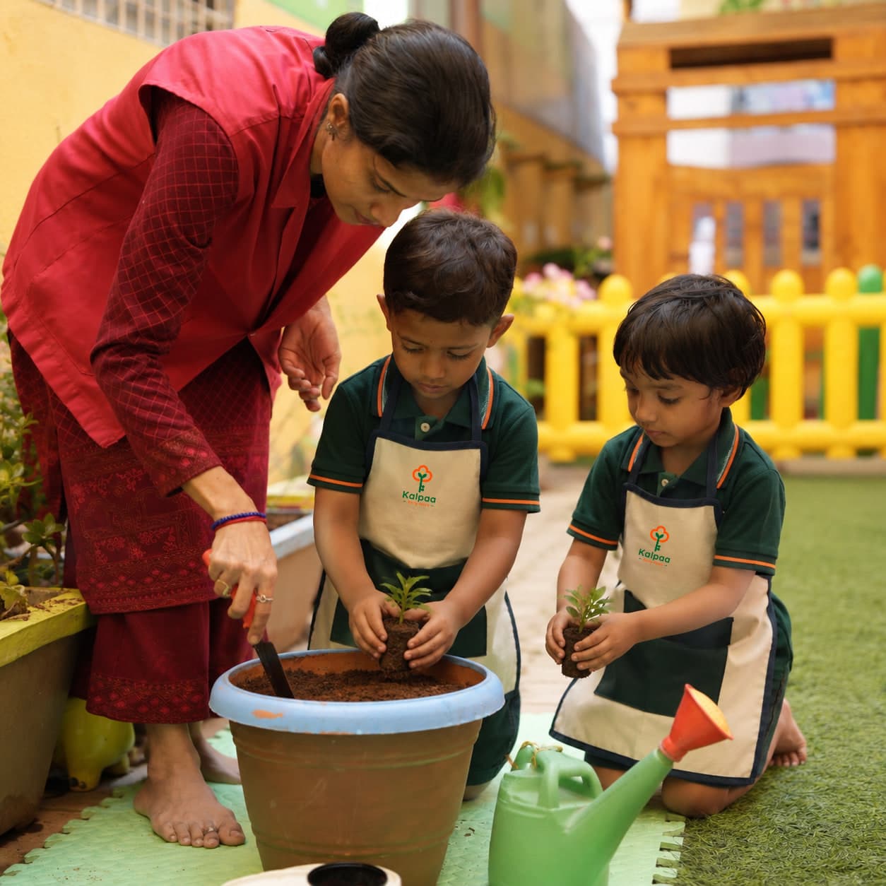 A teacher and two children planting seedlings together