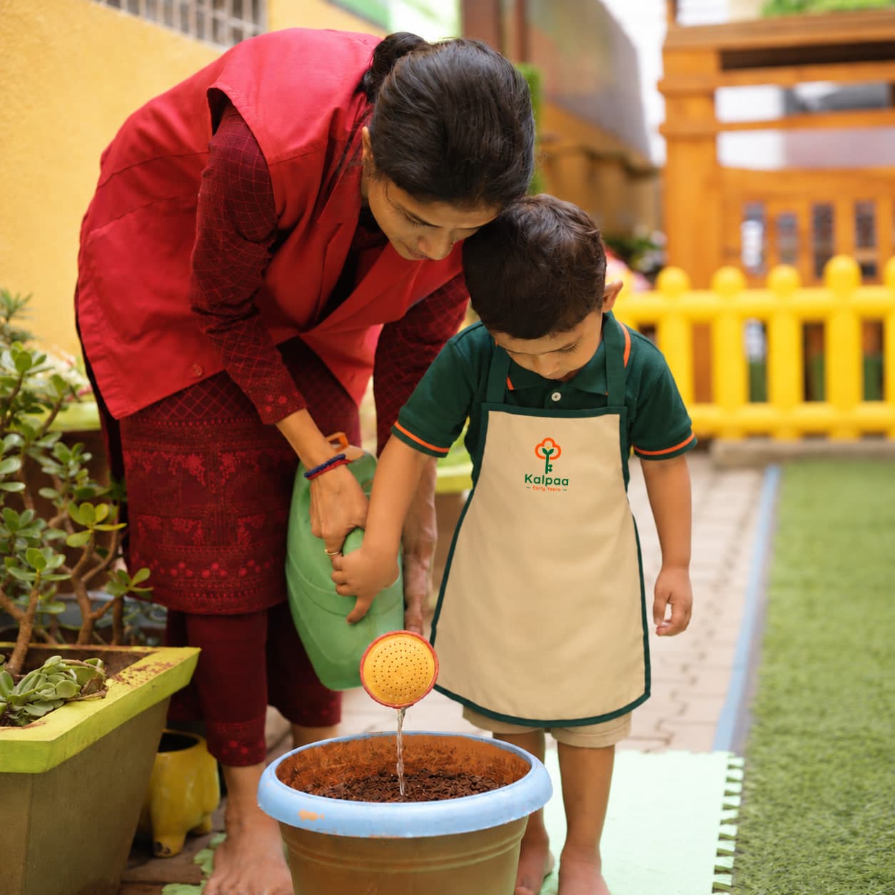 A teacher and child watering a pot together