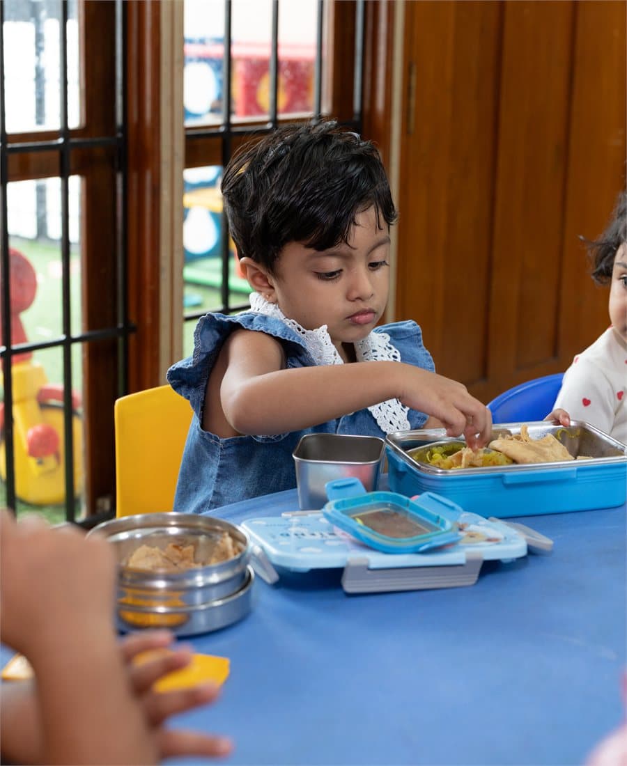 A Kalpaa child eating lunch from her tiffin at the daycare table